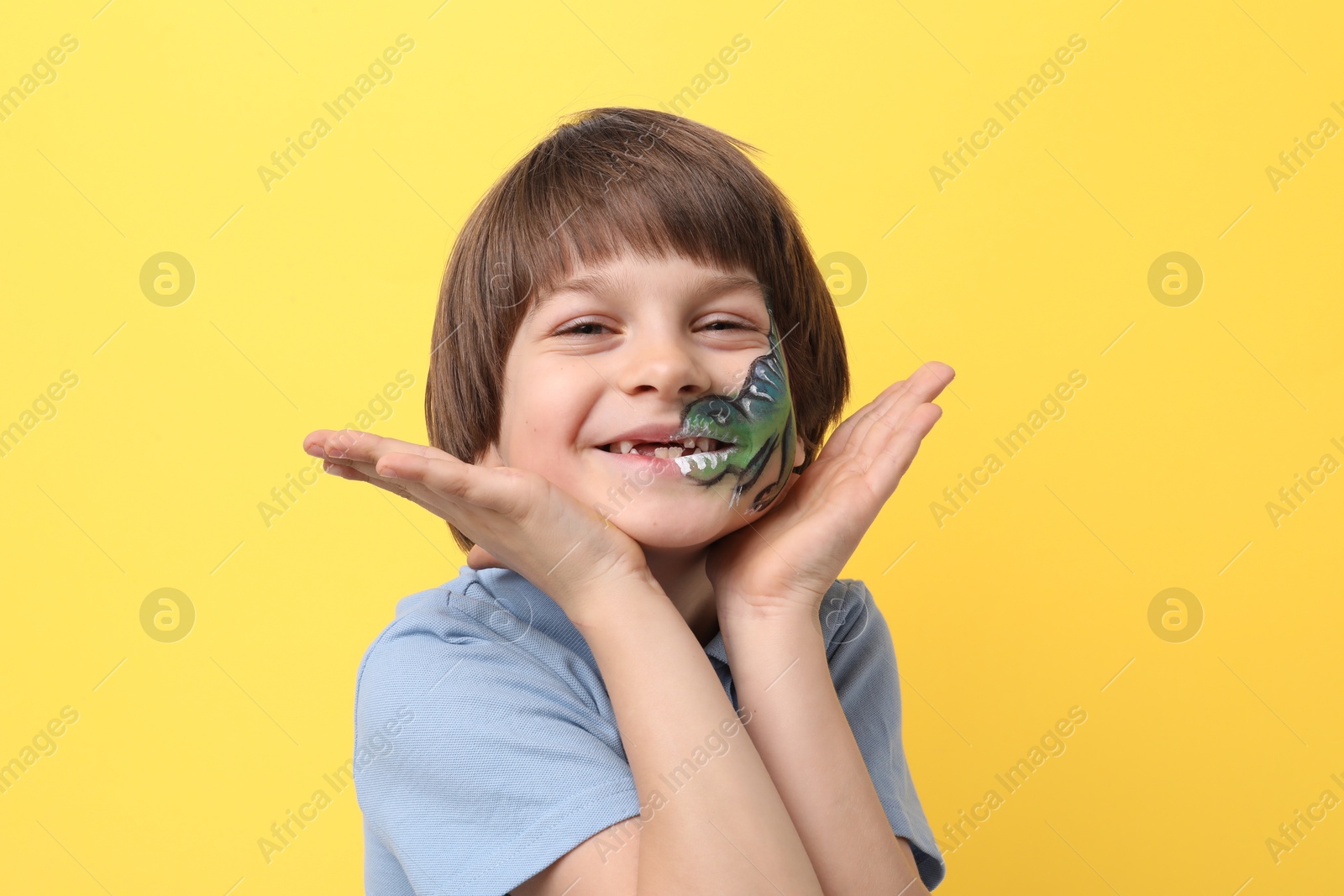 Cute boy with dinosaur face painting on yellow background Photo of Cute boy with dinosaur face painting on yellow background