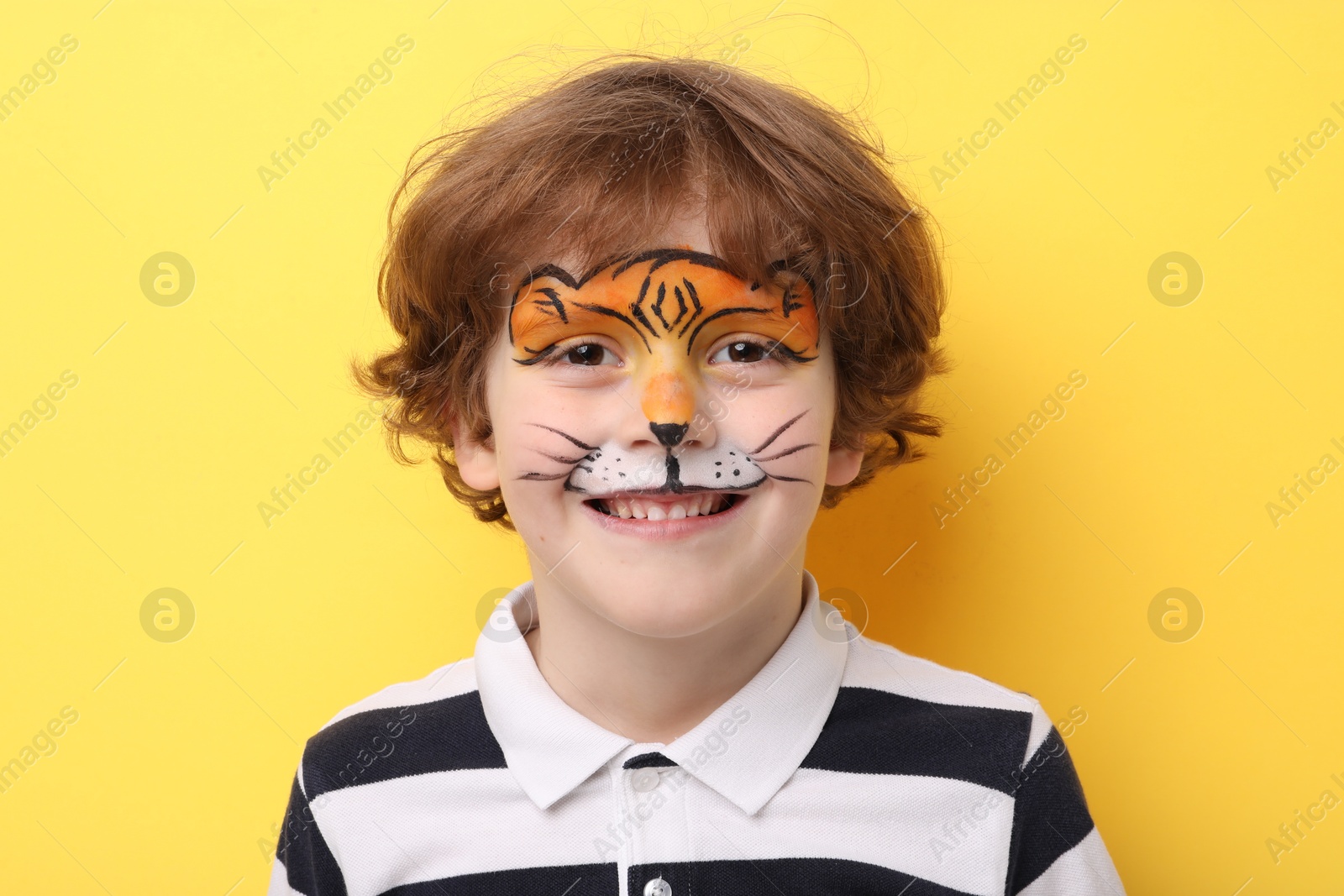 Cute boy with tiger face painting on yellow background Photo of Cute boy with tiger face painting on yellow background