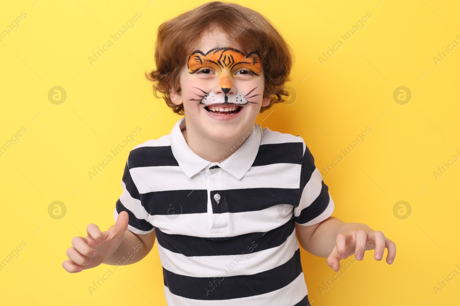 Cute boy with tiger face painting posing on yellow background Photo of Cute boy with tiger face painting posing on yellow background