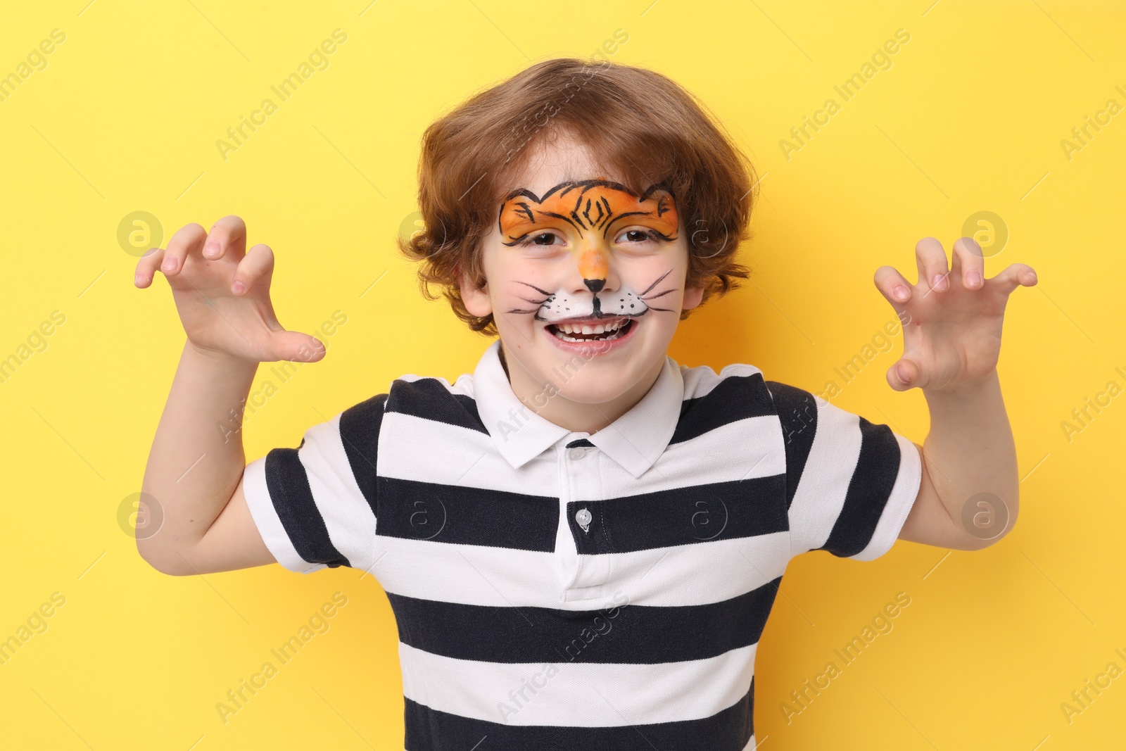 Cute boy with tiger face painting posing on yellow background Photo of Cute boy with tiger face painting posing on yellow background