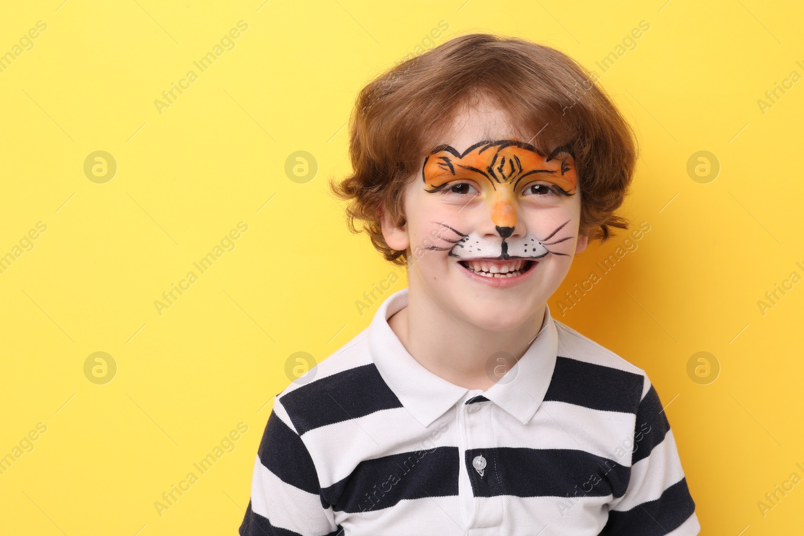 Cute boy with tiger face painting on yellow background, space for text Photo of Cute boy with tiger face painting on yellow background, space for text