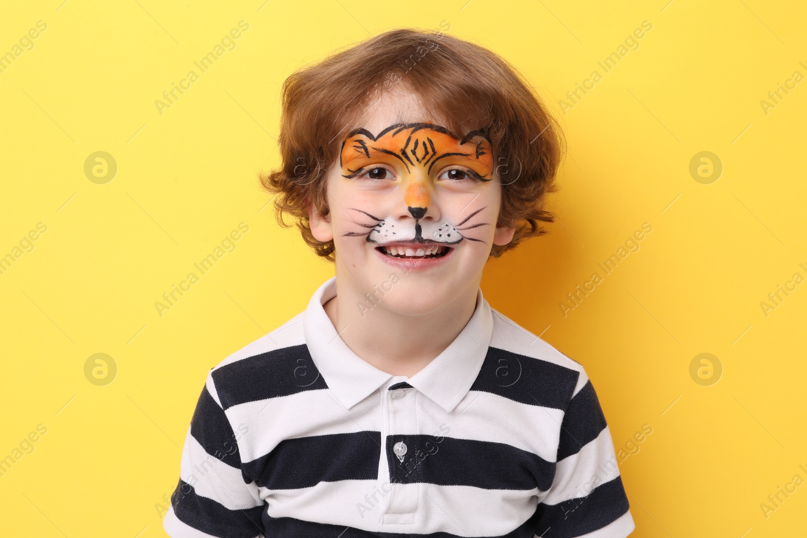 Cute boy with tiger face painting on yellow background Photo of Cute boy with tiger face painting on yellow background