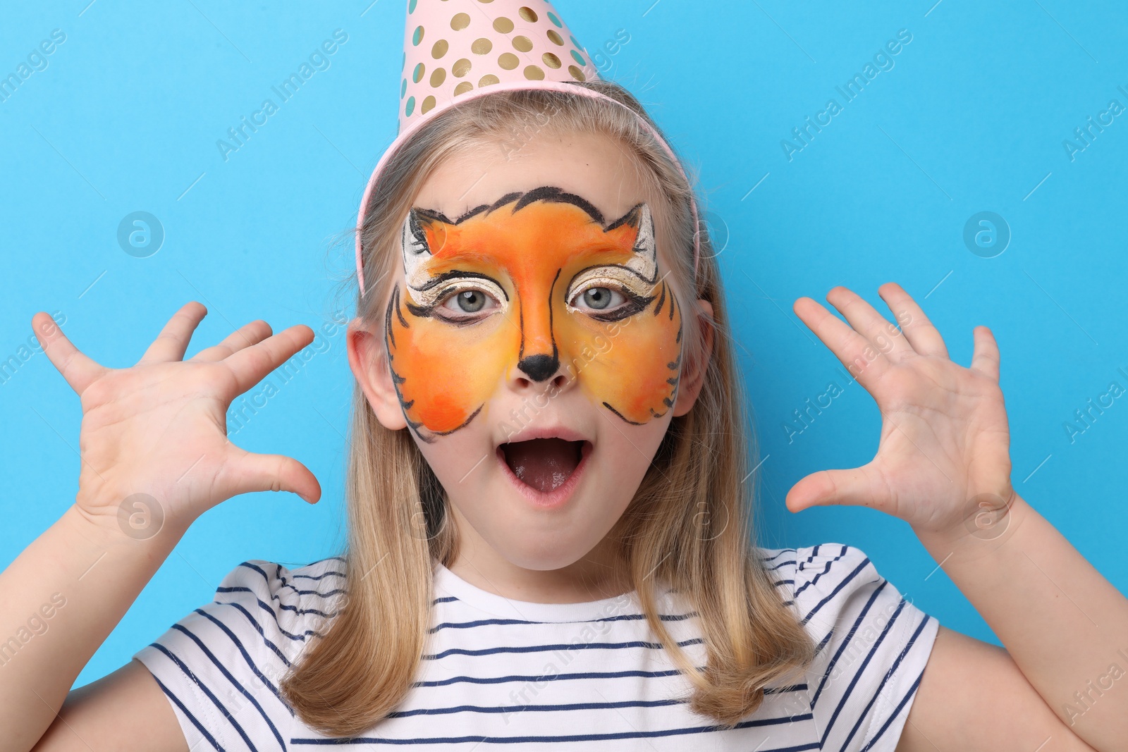 Emotional girl with fox face painting and party hat on light blue background Photo of Emotional girl with fox face painting and party hat on light blue background