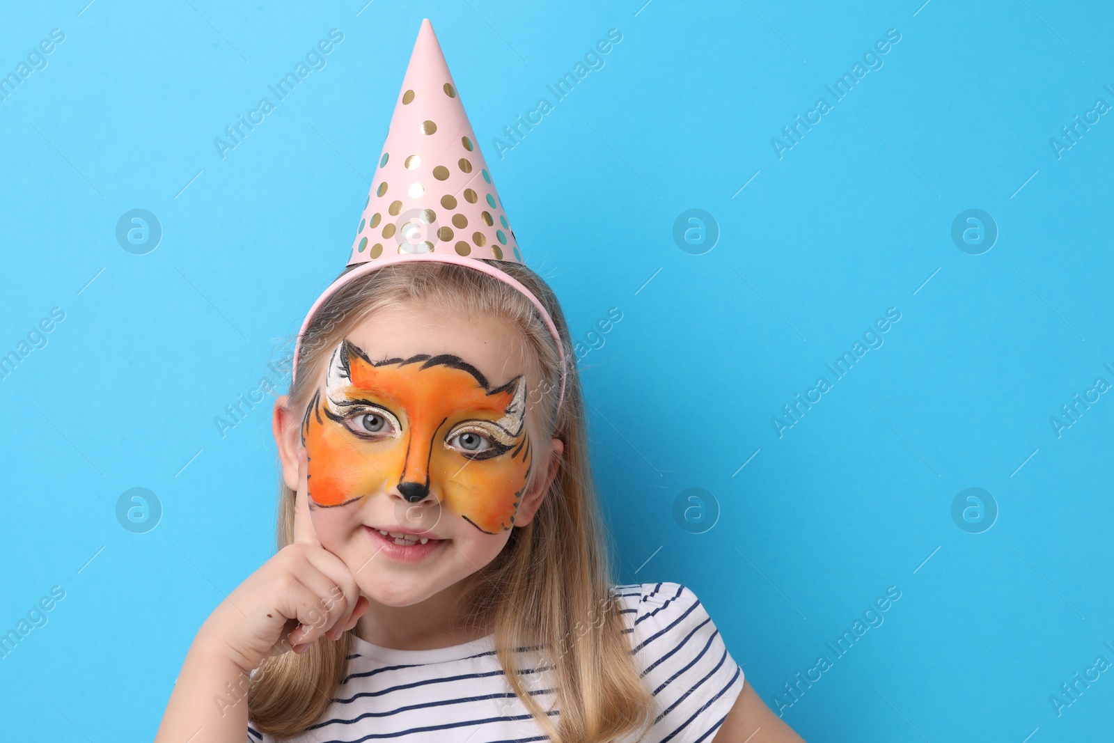 Cute girl with fox face painting and party hat on light blue background, space for text Photo of Cute girl with fox face painting and party hat on light blue background, space for text