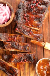 Photo of Delicious spare ribs, onion, sauce and brush on wooden table, flat lay