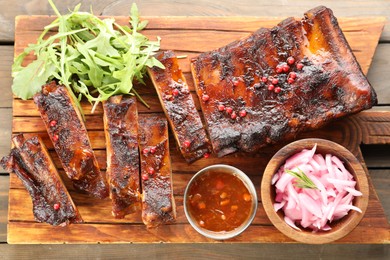 Photo of Delicious spare ribs, sauce, arugula and onion on wooden table, top view