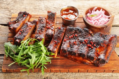 Photo of Delicious spare ribs, onion, sauce and arugula on wooden table