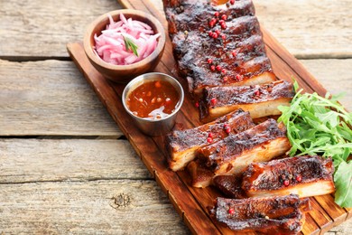 Photo of Delicious spare ribs, onion, sauce and arugula on wooden table