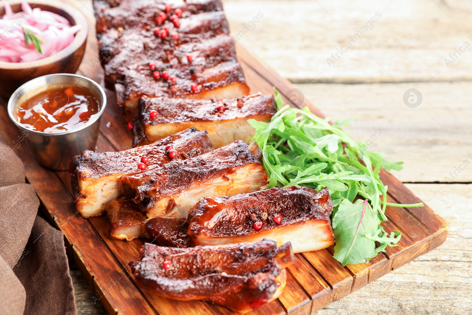 Delicious spare ribs, sauce and arugula on wooden table, closeup Photo of Delicious spare ribs, sauce and arugula on wooden table, closeup