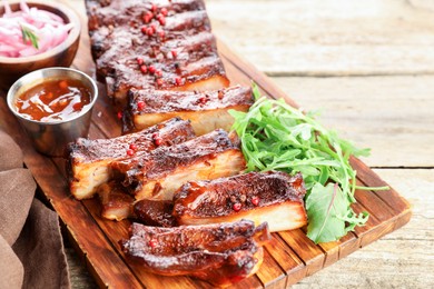 Photo of Delicious spare ribs, sauce and arugula on wooden table, closeup