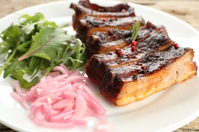Photo of Delicious spare ribs, onion and arugula on wooden table, closeup