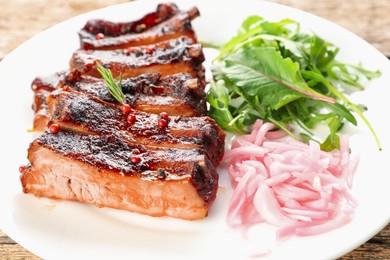 Photo of Delicious spare ribs, onion and arugula on wooden table, closeup