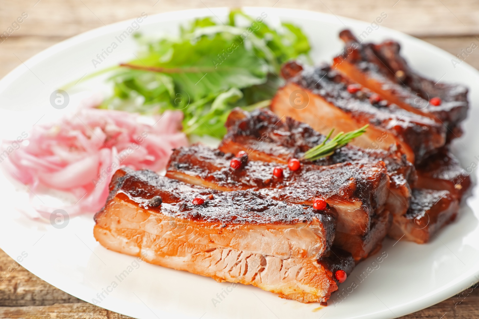 Delicious spare ribs, onion and arugula on wooden table, closeup Photo of Delicious spare ribs, onion and arugula on wooden table, closeup