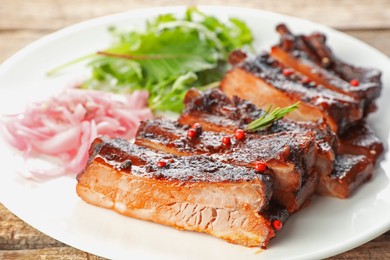 Photo of Delicious spare ribs, onion and arugula on wooden table, closeup