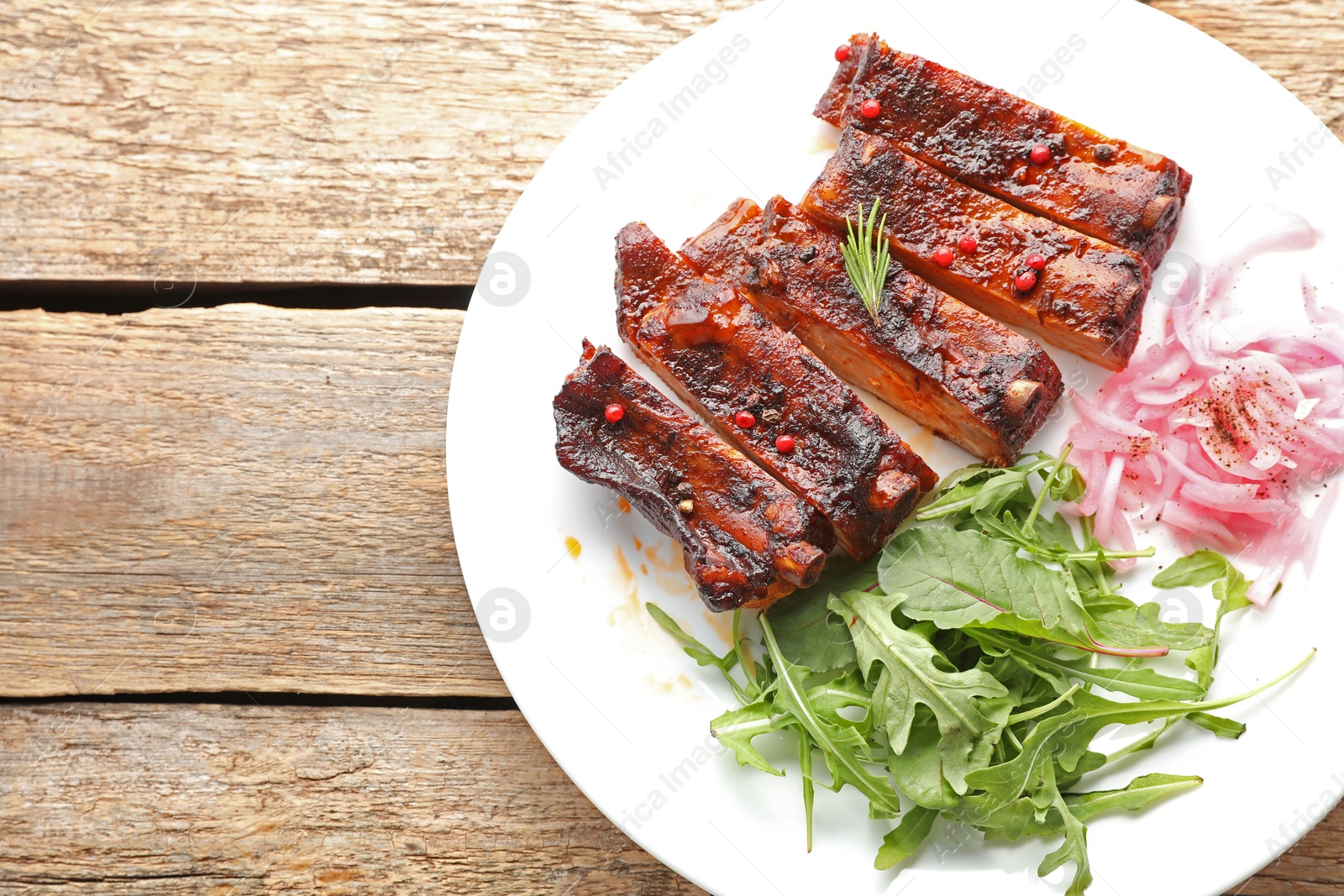 Delicious spare ribs, onion and arugula on wooden table, top view. Space for text Photo of Delicious spare ribs, onion and arugula on wooden table, top view. Space for text