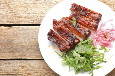 Photo of Delicious spare ribs, onion and arugula on wooden table, top view. Space for text