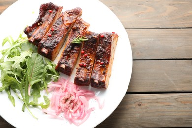 Photo of Delicious spare ribs, onion and arugula on wooden table, top view. Space for text