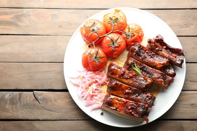 Photo of Delicious spare ribs, onion and sun dried tomatoes on wooden table, top view. Space for text