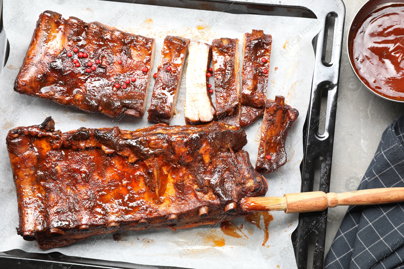 Delicious spare ribs, sauce and brush on grey table, flat lay Photo of Delicious spare ribs, sauce and brush on grey table, flat lay