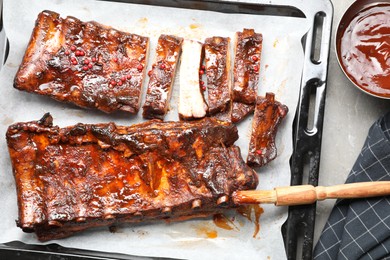 Photo of Delicious spare ribs, sauce and brush on grey table, flat lay