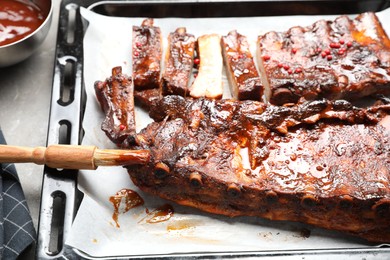 Photo of Delicious spare ribs, sauce and brush on grey table, closeup