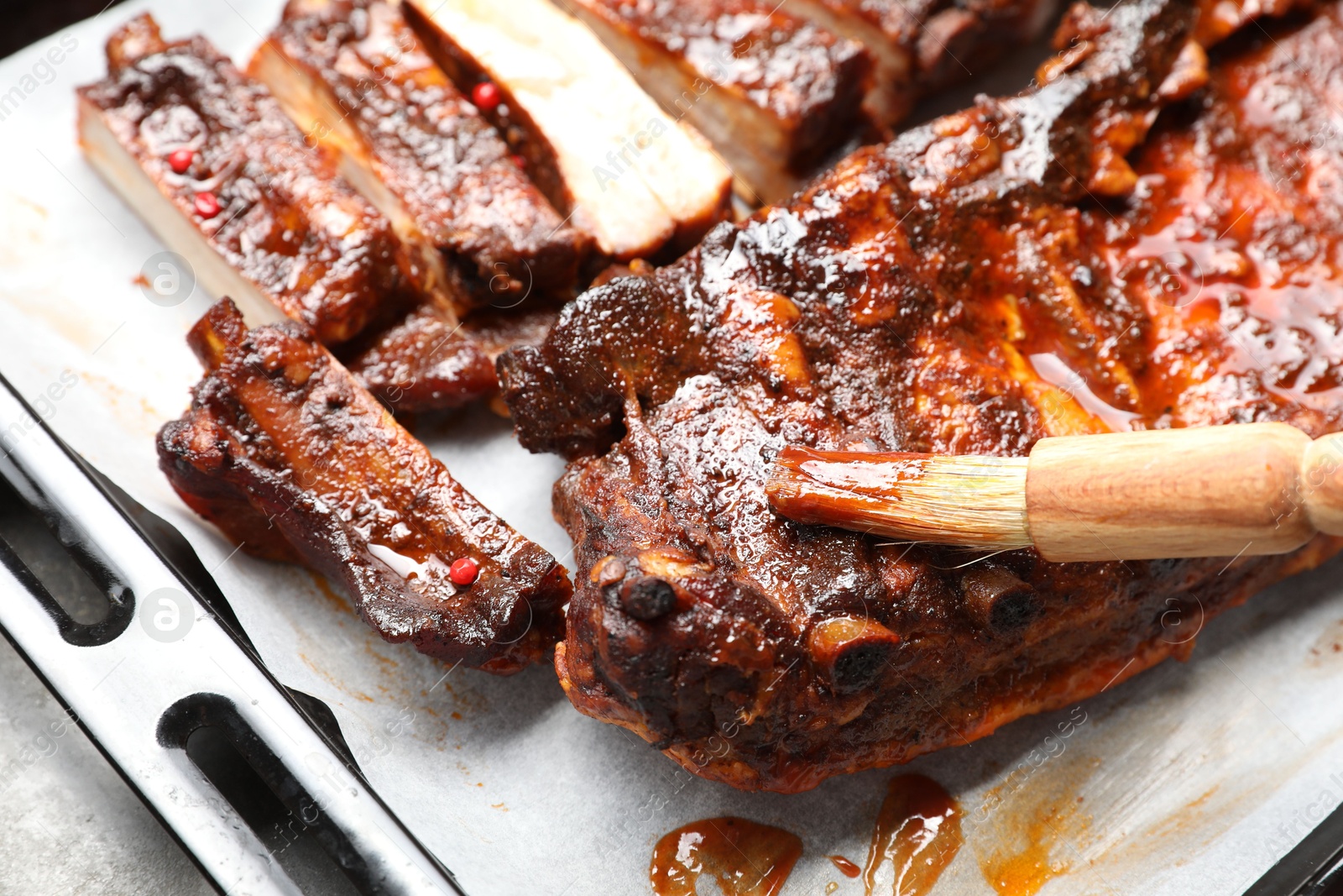 Spreading sauce with brush onto delicious spare ribs at grey table, closeup Photo of Spreading sauce with brush onto delicious spare ribs at grey table, closeup