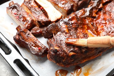 Photo of Spreading sauce with brush onto delicious spare ribs at grey table, closeup