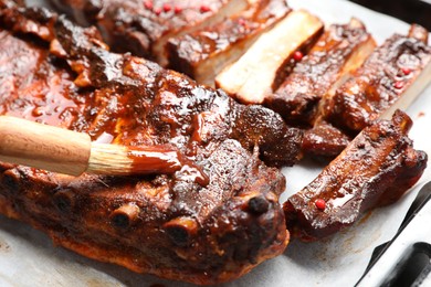 Photo of Spreading sauce with brush onto delicious spare ribs at baking tray, closeup