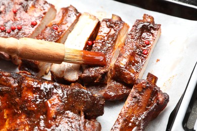 Photo of Spreading sauce with brush onto delicious spare ribs at baking tray, closeup