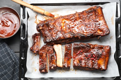 Photo of Delicious spare ribs, sauce and brush on grey wooden table, flat lay