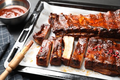 Photo of Delicious spare ribs, sauce and brush on grey table, closeup