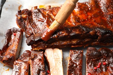 Photo of Spreading sauce with brush onto delicious spare ribs at parchment paper, closeup