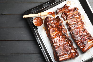 Photo of Delicious spare ribs, sauce and brush on grey wooden table, top view