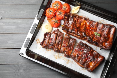 Photo of Delicious spare ribs, baked onion and sun dried tomatoes on grey wooden table, top view