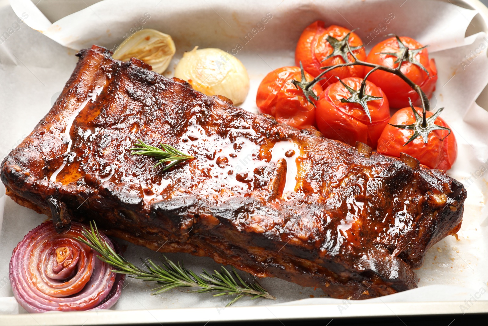 Delicious spare ribs, rosemary, baked onion and sun dried tomatoes on parchment paper, closeup Photo of Delicious spare ribs, rosemary, baked onion and sun dried tomatoes on parchment paper, closeup