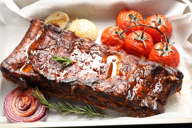 Photo of Delicious spare ribs, rosemary, baked onion and sun dried tomatoes on parchment paper, closeup