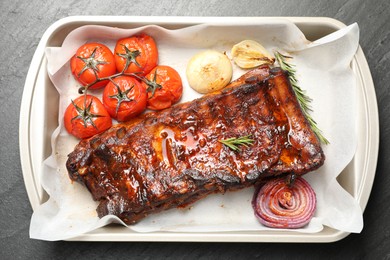 Photo of Delicious spare ribs, rosemary, baked onion and sun dried tomatoes on grey textured table, top view