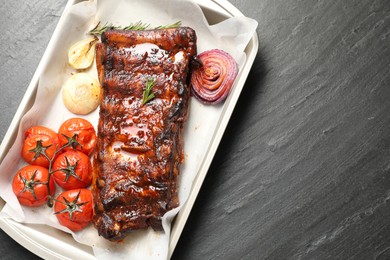 Photo of Delicious spare ribs, rosemary, baked onion and sun dried tomatoes on grey textured table, top view. Space for text