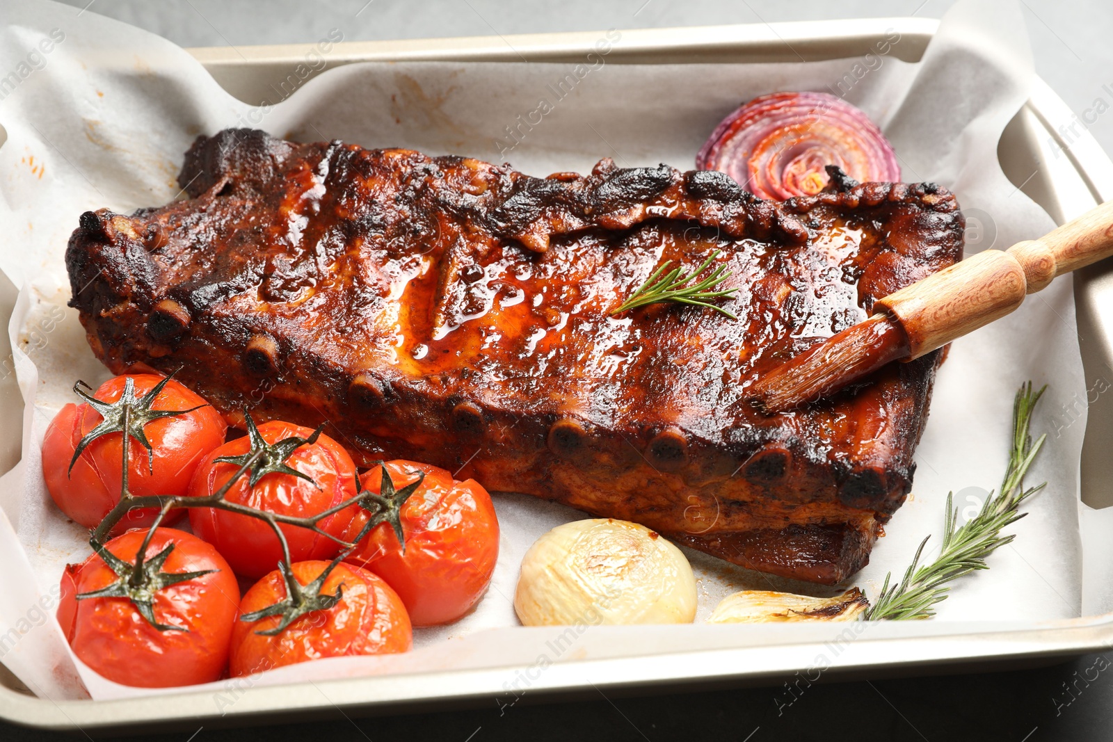 Delicious spare ribs, rosemary, baked onion and sun dried tomatoes on grey table, closeup Photo of Delicious spare ribs, rosemary, baked onion and sun dried tomatoes on grey table, closeup