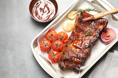 Photo of Delicious spare ribs, rosemary, baked onion, sauce and sun dried tomatoes on grey table, flat lay. Space for text