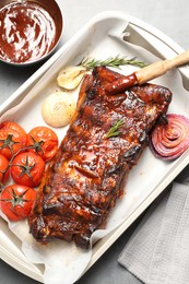 Photo of Delicious spare ribs, rosemary, baked onion, sauce and sun dried tomatoes on grey table, flat lay