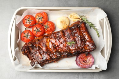 Photo of Delicious spare ribs, rosemary, baked onion and sun dried tomatoes on grey textured table, top view