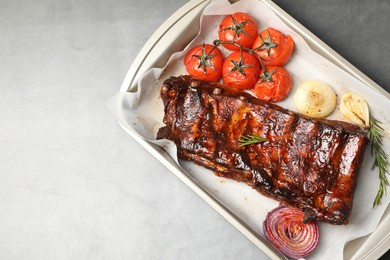 Photo of Delicious spare ribs, rosemary, baked onion and sun dried tomatoes on grey textured table, top view. Space for text