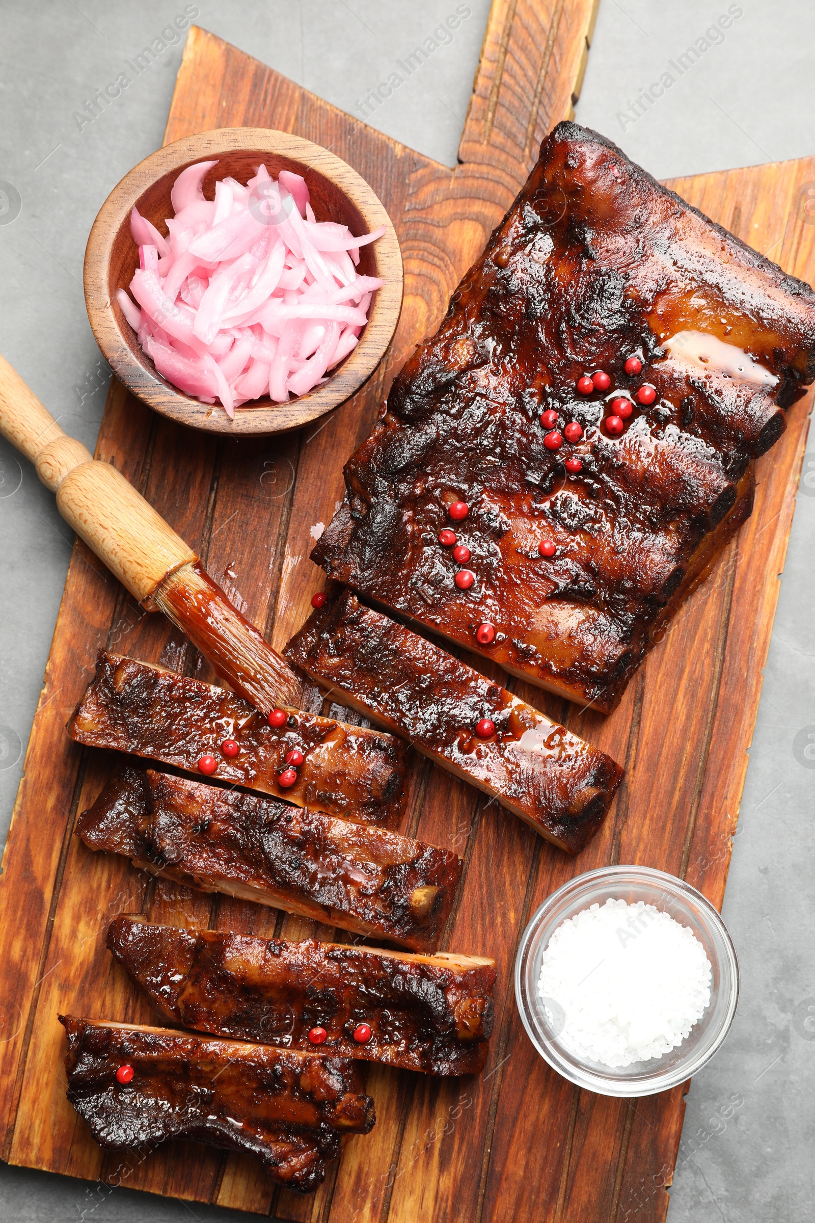 Delicious spare ribs, onion, salt and brush on grey table, top view Photo of Delicious spare ribs, onion, salt and brush on grey table, top view