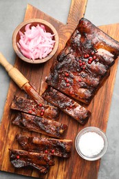 Photo of Delicious spare ribs, onion, salt and brush on grey table, top view