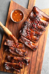 Photo of Delicious spare ribs, sauce and brush on grey table, top view