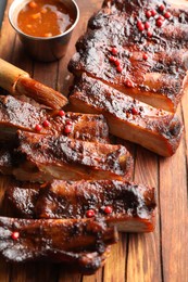 Photo of Delicious spare ribs, sauce and brush on wooden table, closeup