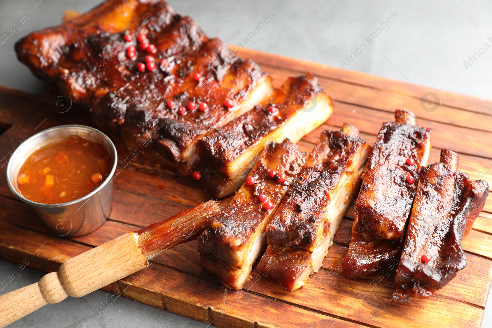 Delicious spare ribs, sauce and brush on grey table, closeup Photo of Delicious spare ribs, sauce and brush on grey table, closeup