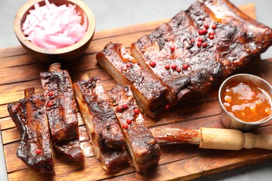 Photo of Delicious spare ribs, sauce and brush on grey table, closeup
