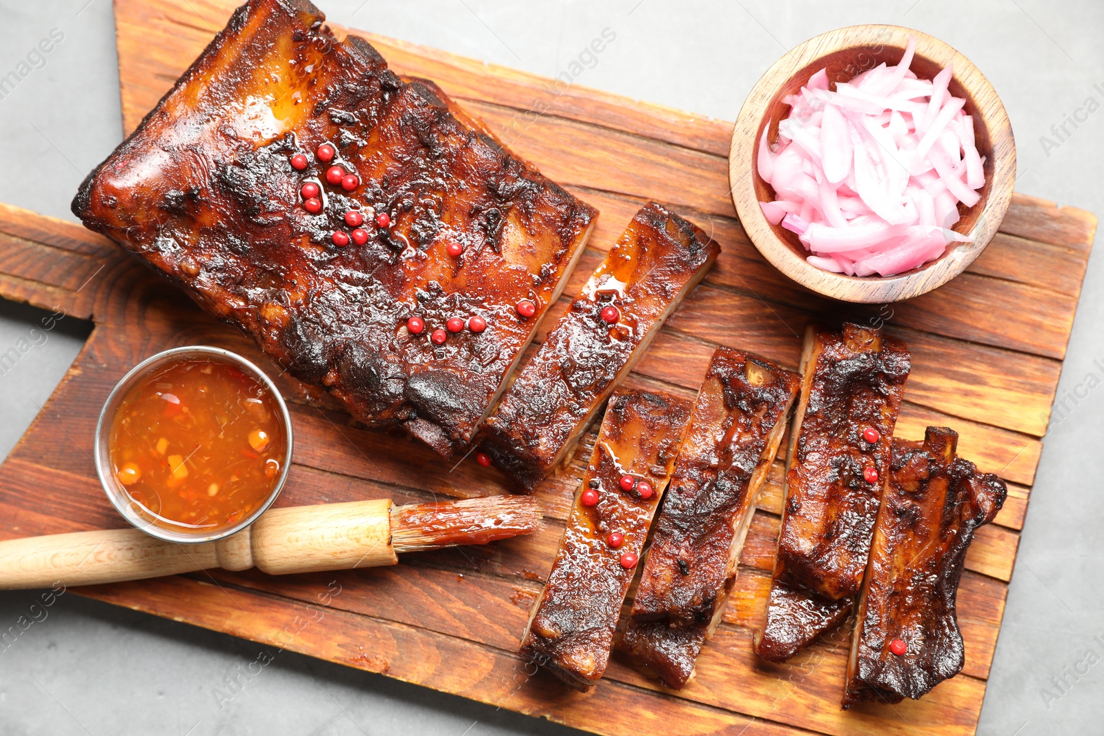 Delicious spare ribs, sauce, onion and brush on grey table, top view Photo of Delicious spare ribs, sauce, onion and brush on grey table, top view